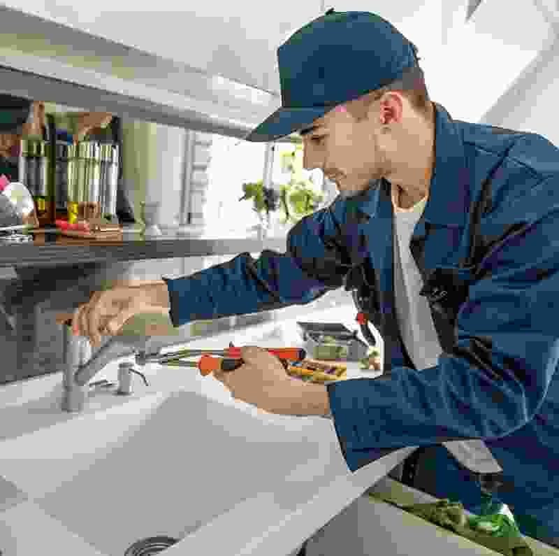 Professional technician installing a faucet in a modern kitchen, showcasing quality handyman services related to plumbing and home maintenance.