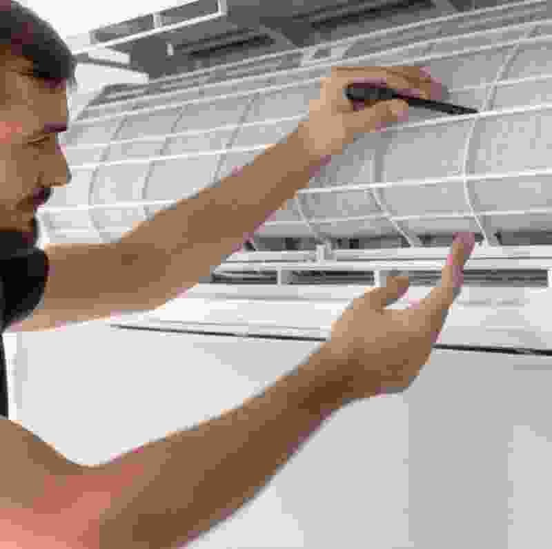 Technician inspecting split air conditioning unit, emphasizing quality installation and maintenance services by Extra Electrical.