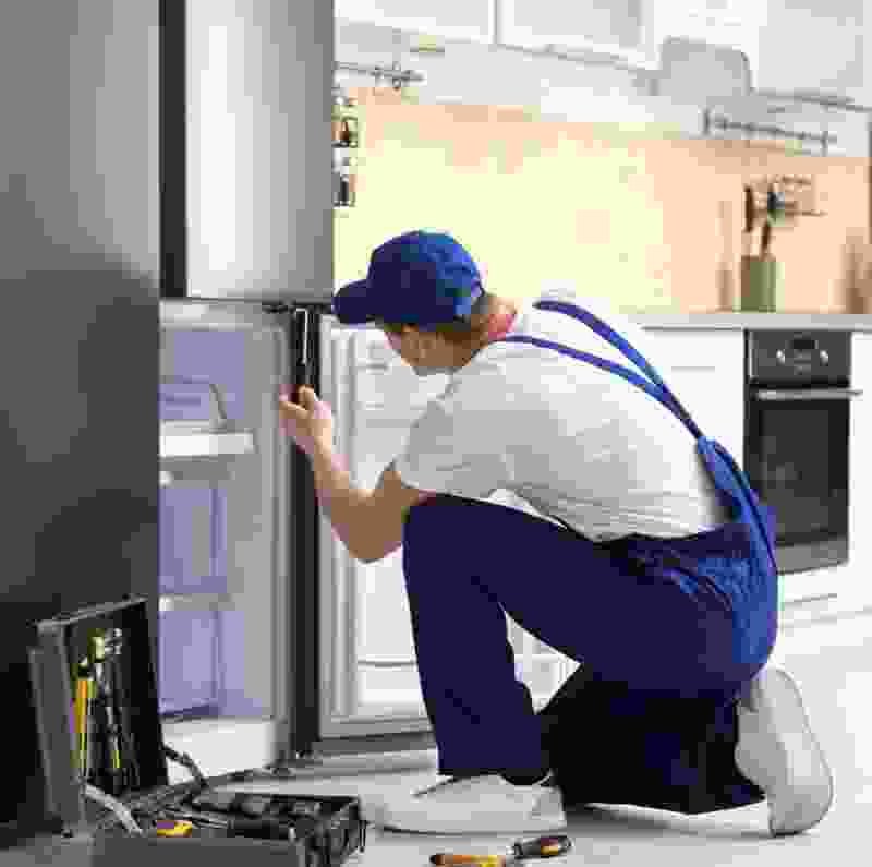 Plumber servicing refrigerator in modern kitchen, tools nearby, highlighting indoor plumbing expertise.