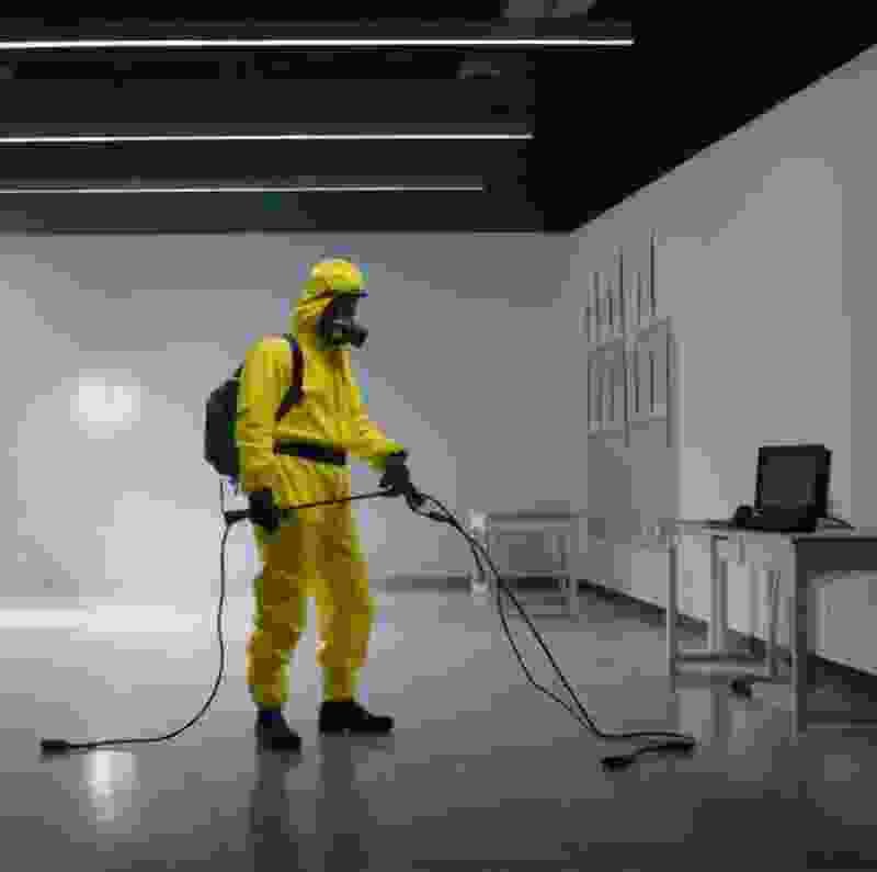 Person in yellow protective suit conducting spray sanitization in a commercial setting, demonstrating Extra Electrical's 24/7 sanitization service for cleanliness and safety.