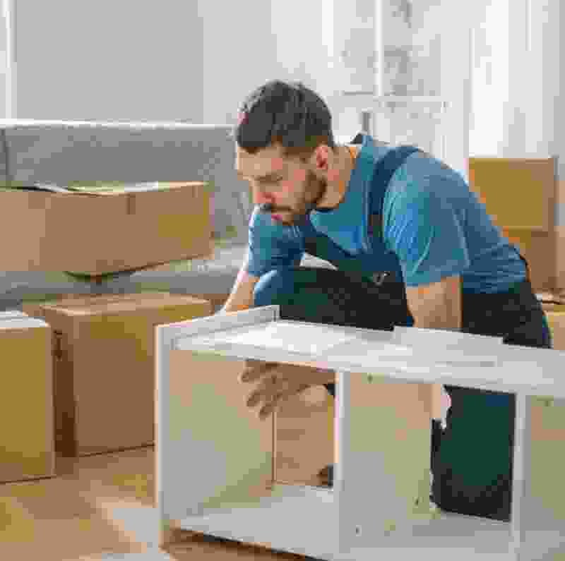 Man assembling furniture in a room filled with moving boxes, showcasing carpentry and handyman services by Extra Electrical.